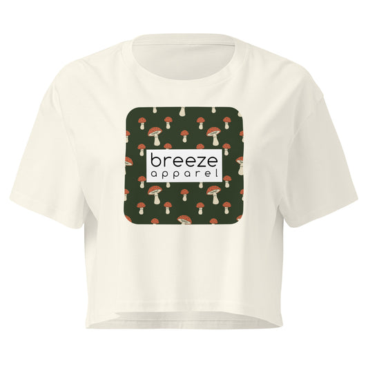 Cream crop top with graphic of mushrooms set on a green background and overlaid with a white rectangle logo.