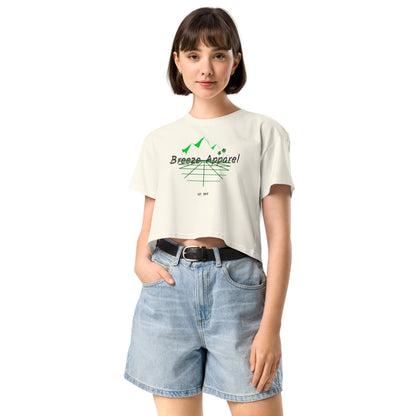 Woman wearing cream crop top with graphic of palm trees and mountains.