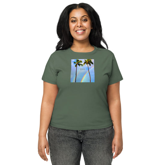 Woman wearing pine-green t-shirt with a graphic of palm trees, rainbow, and a clear blue sky in the background. A small, black 'breeze apparel' logo is between the trees.