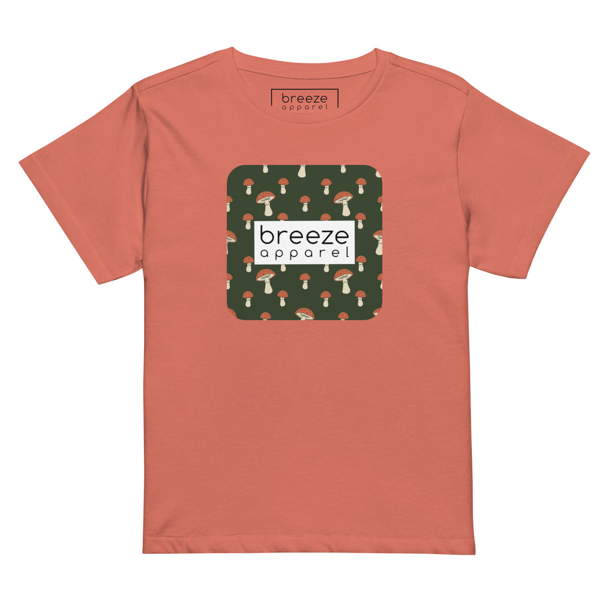 Red-orange t-shirt with design of mushrooms set on green background and overlaid with a white rectangle with 'breeze apparel' in black inside.
