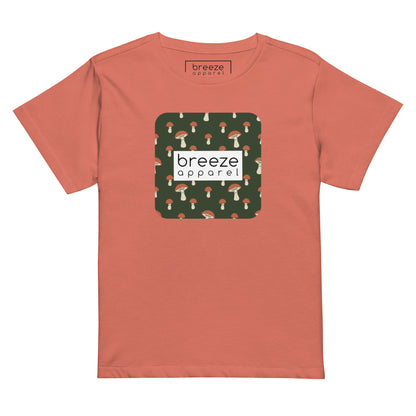 Red-orange t-shirt with design of mushrooms set on green background and overlaid with a white rectangle with 'breeze apparel' in black inside.