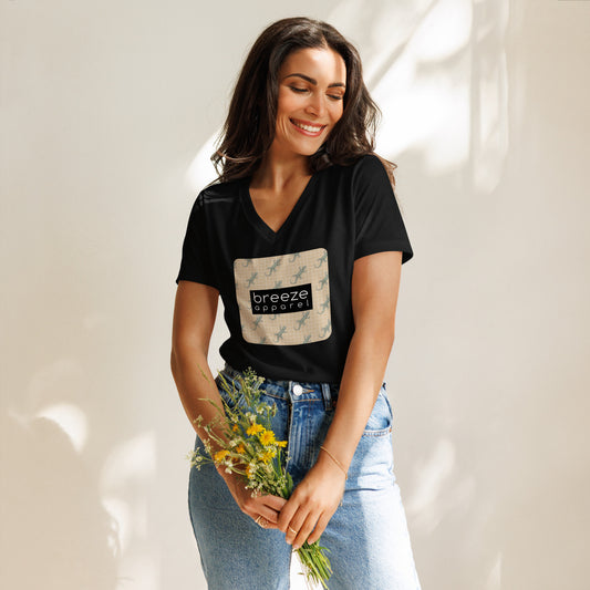 Woman wearing black t-shirt with square over chest that contains pattern of green geckos set on beige background, overlaid with black, rectangular logo with white lettering.